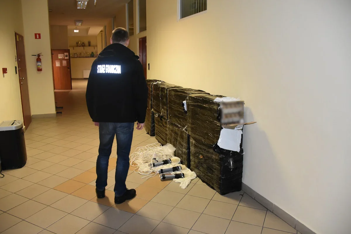 Funkcionariusz Straży Granicznej stoi w korytarzu obok dużych, owiniętych taśmą pakunków i rozłożonych przedmiotów.