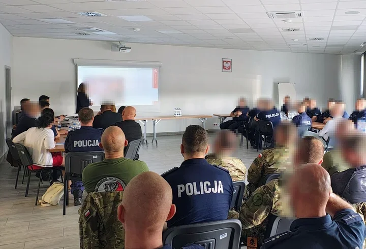 Funkcjonariusze policji i wojska siedzą w sali szkoleniowej podczas prezentacji wyświetlanej na ekranie projektora.