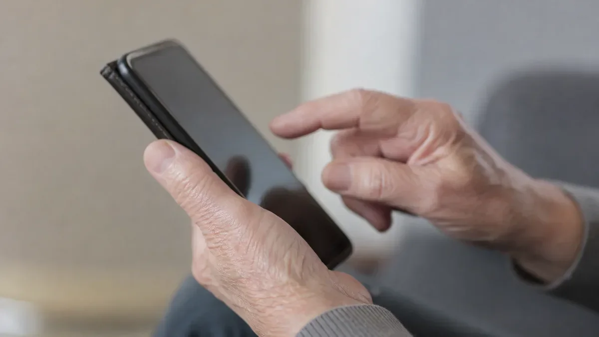 Dłonie starszej osoby trzymającej smartfon i dotykające ekranu.