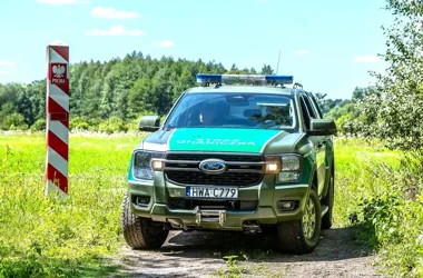 Pojazd Straży Granicznej stoi na polnej drodze przy polskim słupku granicznym w zielonym, leśnym terenie.