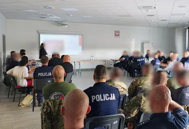 Funkcjonariusze policji i wojska siedzą w sali szkoleniowej podczas prezentacji wyświetlanej na ekranie projektora.
