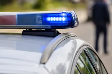 Błękitny sygnalizator świetlny na dachu policyjnego radiowozu, w tle rozmyta postać przechodnia.