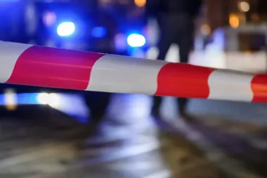 Czerwono-biała taśma policyjna na tle błękitnych świateł w nocy.