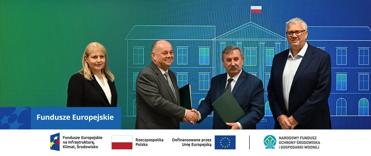 Cztery osoby stoją przed banerem z napisami o funduszach europejskich, dwie mężczyzny w środku uściskają sobie dłonie i trzymają teczki.